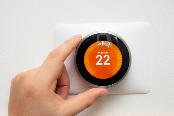 A person turning a smart thermostat dial.